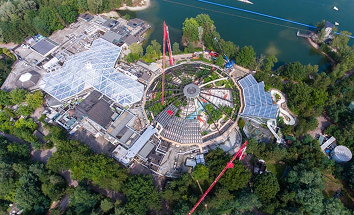 Aerial view of a circular building under construction with cranes and glass roof