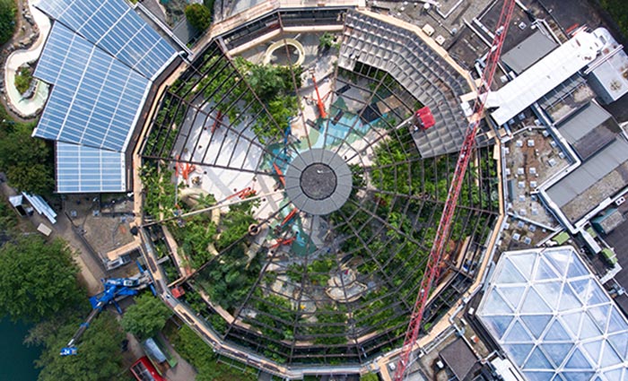 Luchtfoto van een grote glazen koepelstructuur omgeven door groen