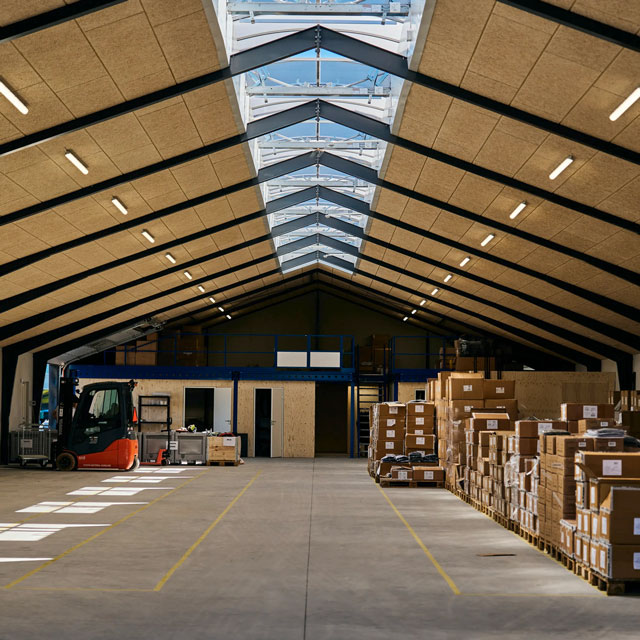 En rummelig lagerhal, der får lys ind gennem VELUX-tagvinduer i tagryggen og er fyldt med paller med kasser.