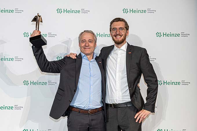 Zwei Kollegen von VELUX Commercial und VELUX Deutschland, die stolz die goldene Trophäe in die Luft halten. 