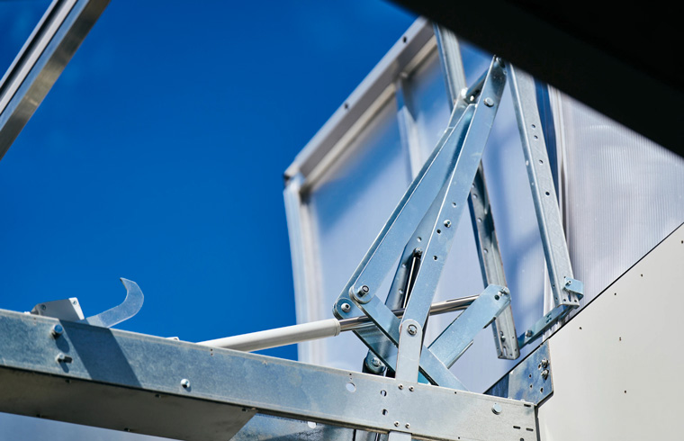 Detail of open VELUX flat roof window mechanism against clear blue sky.