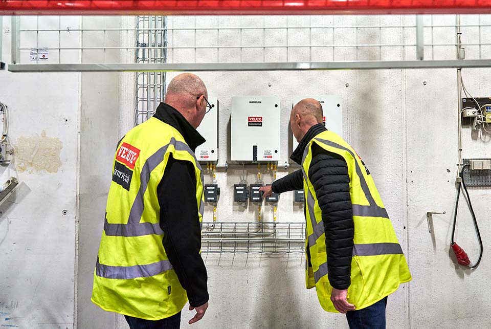 To teknikere i sikkerhedsveste inspicerer styretavlen til brandventilationsanlægget.
