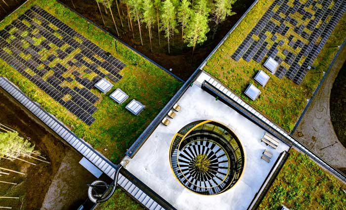 Luftfoto av et grønt tak med solcellepaneler montert på et miljøvennlig kontorbygg omgitt av skog.