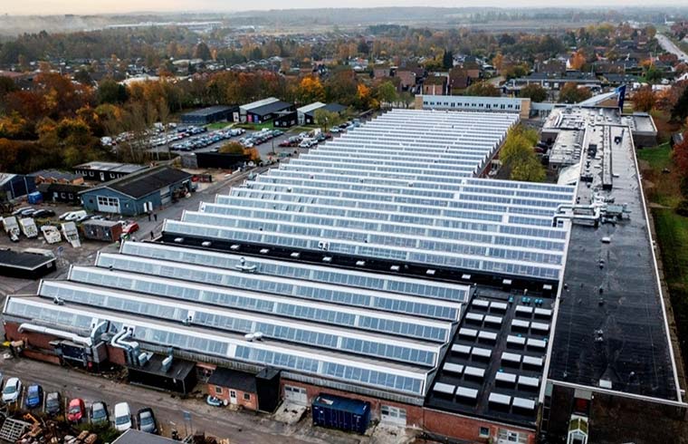 Luftfoto af Hillerød Tekniske Skole med lange rækker af ovenlysvinduer i en efterårsby