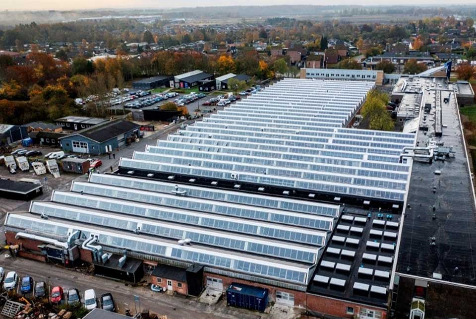 Luftfoto af Hillerød Tekniske Skole med lange rækker af ovenlysvinduer i en efterårsby
