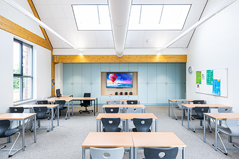 Klaslokaal met een schuin plafond, VELUX dakramen, bureaus en een scherm. Foto: Kasper Veenstra