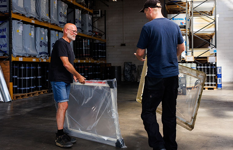 Werknemers in een magazijn die materialen verwerken, zichtbare dakspanten en dakramen boven hen