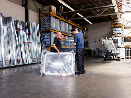 Werknemers in een magazijn die materialen verwerken, zichtbare dakspanten en dakramen boven hen