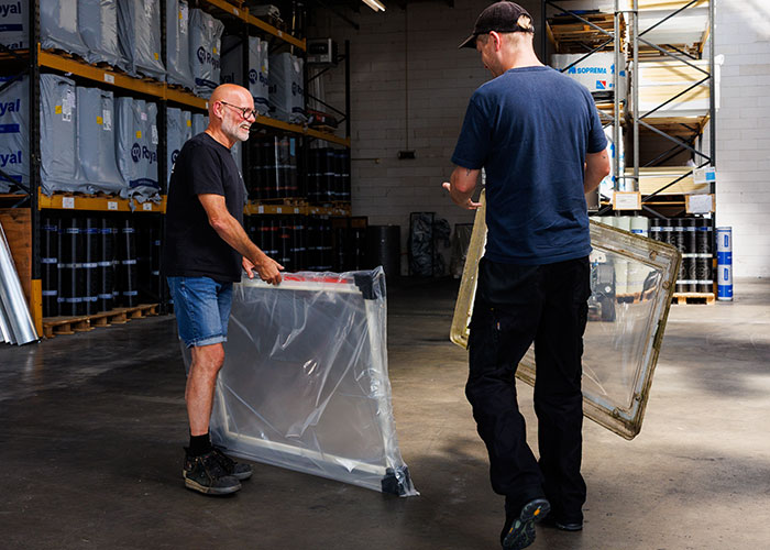 Werknemers in een magazijn die materialen verwerken, zichtbare dakspanten en dakramen boven hen
